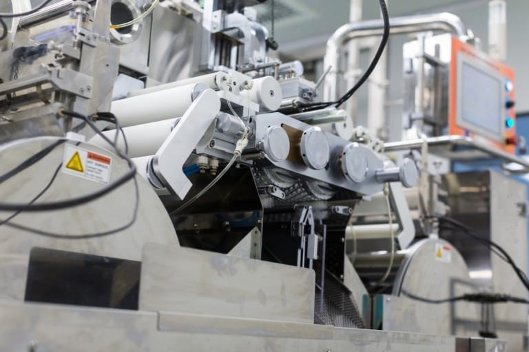 Packaging system Close-up of a big steel chromed manufacture machine with rollers and warning label.
